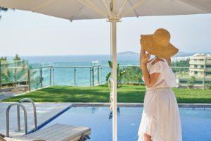 Frau mit einem Hut am Beckenrand mit Blick aufs Meer